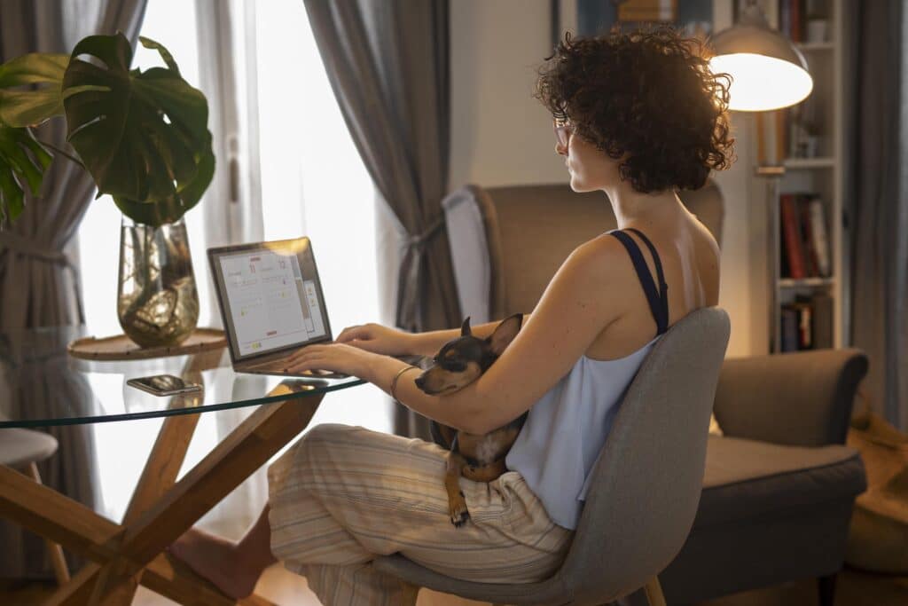 Mulher sentada com seu pet no colo enquanto trabalha no computador.